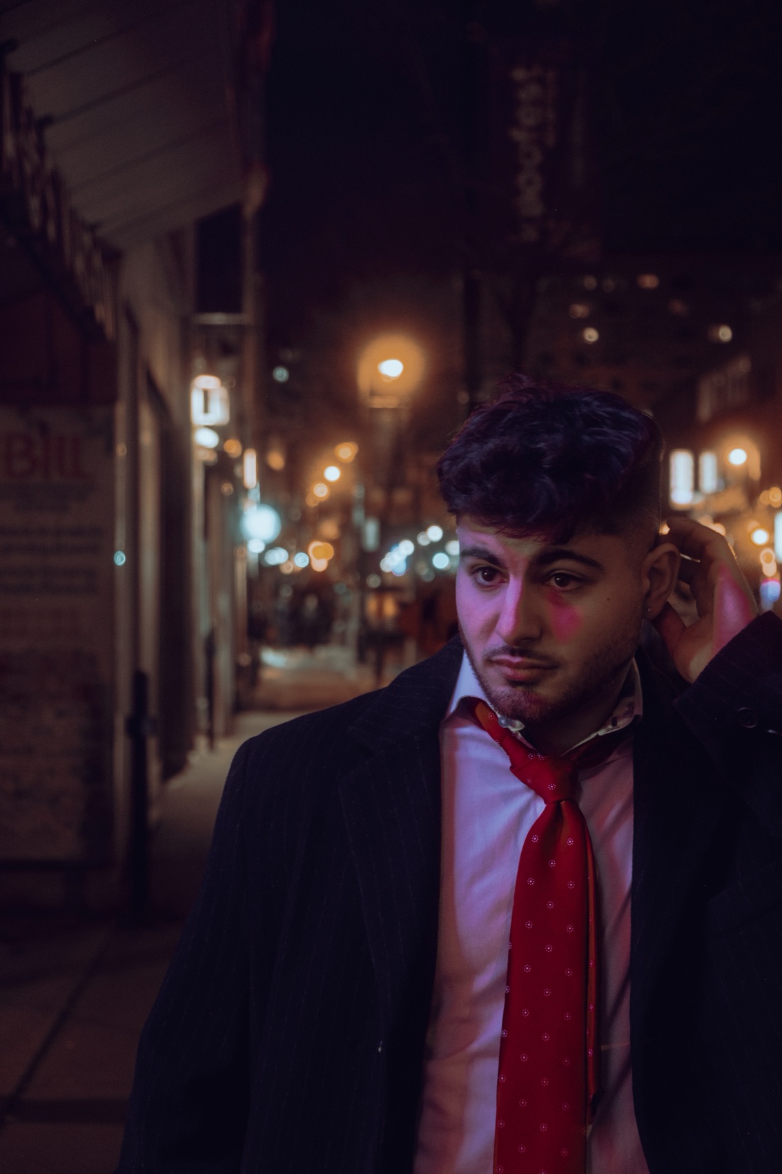 Antony alone on a street at night in a loose red tie.