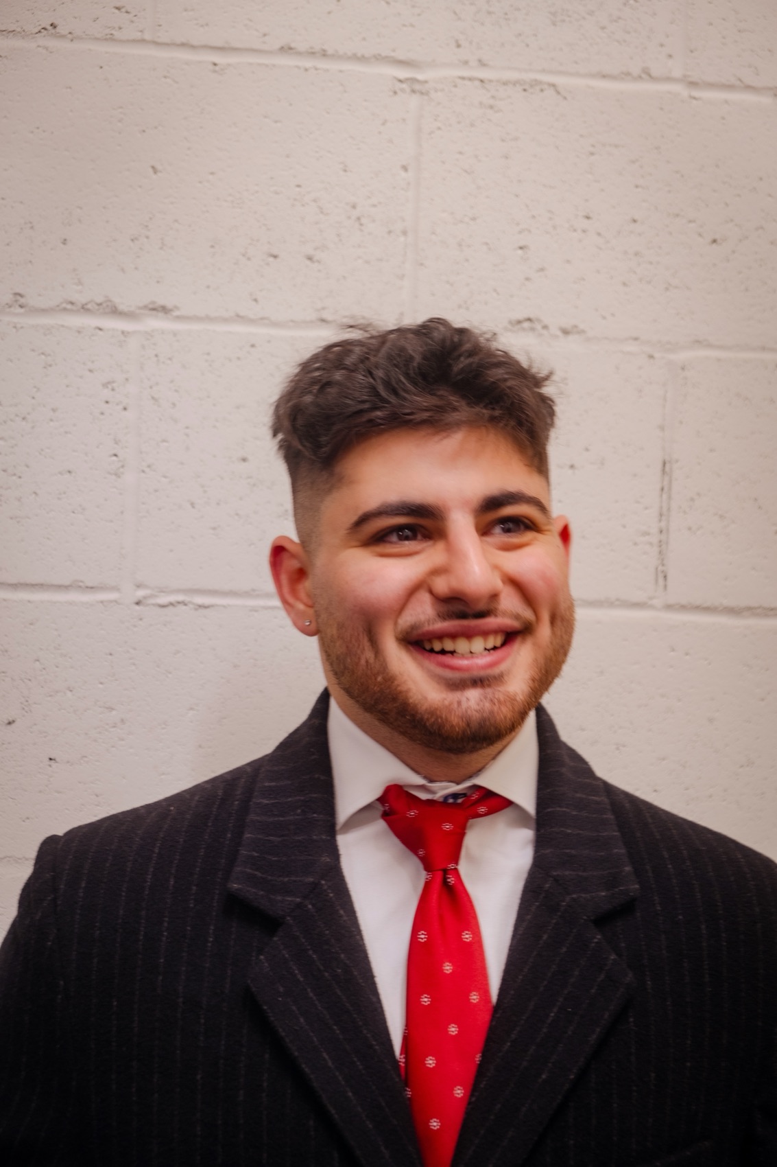Antony in a pinstripe suit and red tie, smiling.